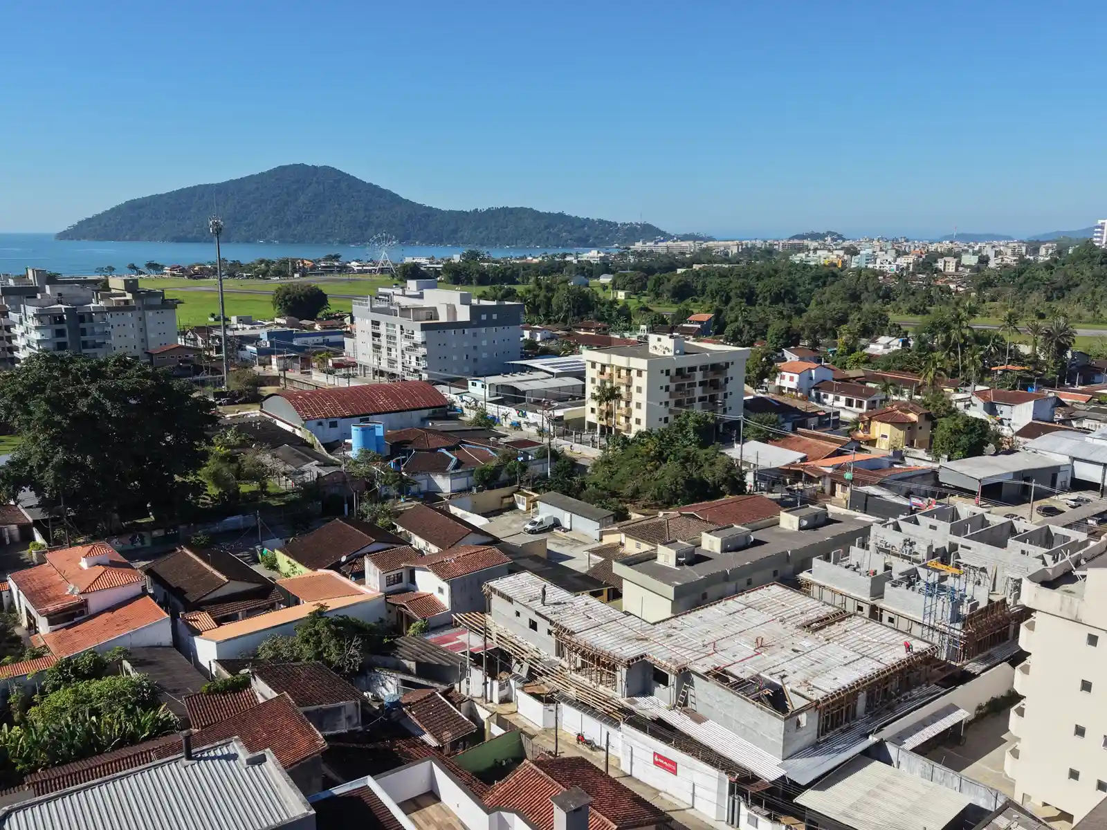 Vista aérea de uma obra em andamento em área urbana de Ubatuba, com o mar e morros ao fundo