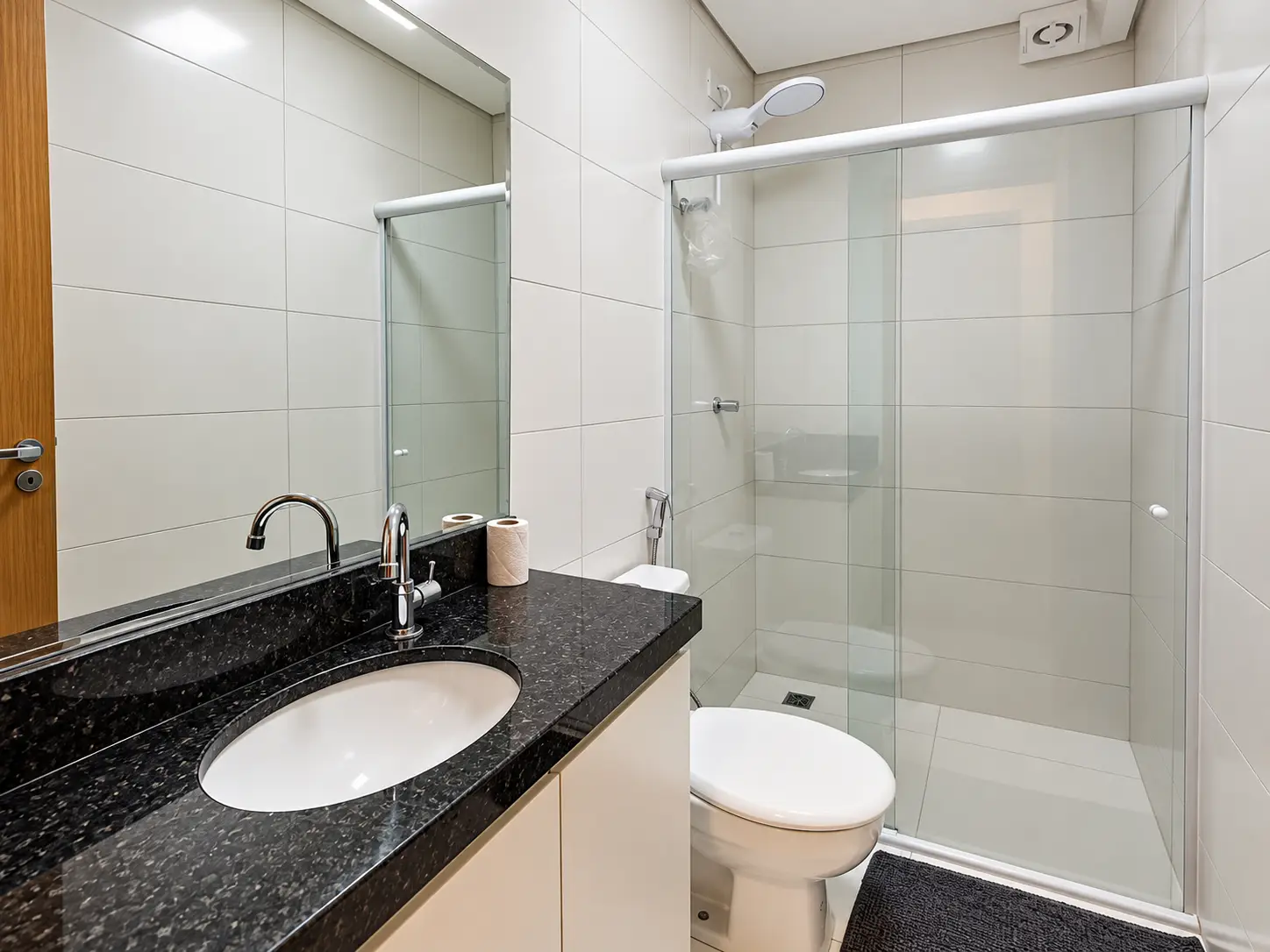 apartamento-itagua-66m2-lg116-banheiro Banheiro com bancada escura, cuba, vaso sanitário e box de vidro.