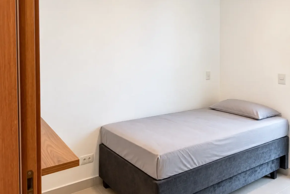 Dormitório do apartamento no Itaguá com cama de casal cinza e paredes claras.