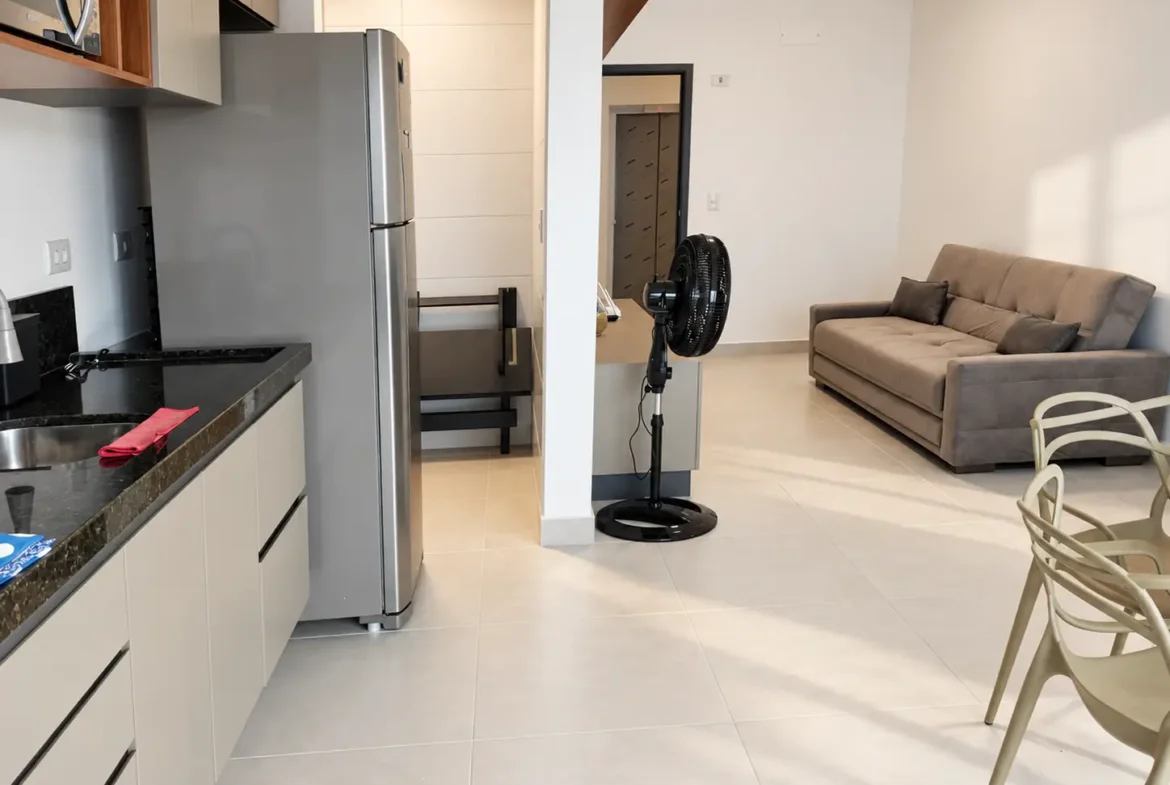 Sala de estar com sofá cinza, ventilador de coluna e passagem para outros ambientes.