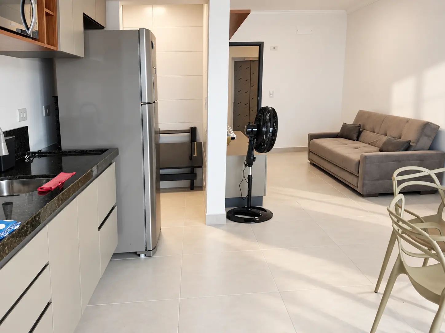 apartamento-itagua-66m2-lg116-sala-integrada Sala de estar com sofá cinza, ventilador de coluna e passagem para outros ambientes.