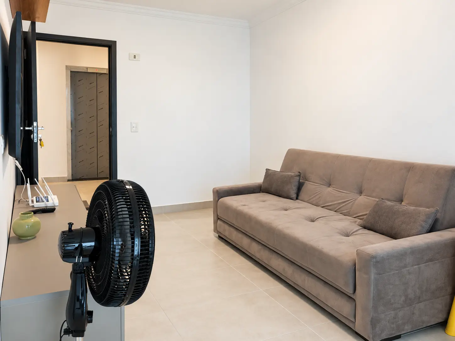 apartamento-itagua-66m2-lg116-sala Vista da cozinha integrada à sala de estar, com sofá e ventilador de coluna.