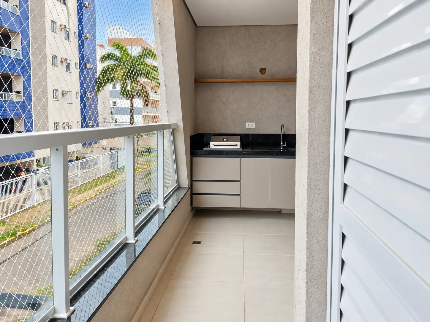apartamento-itagua-66m2-lg116-varanda Sacada do apartamento com guarda-corpo de vidro e vista para edifícios próximos.
