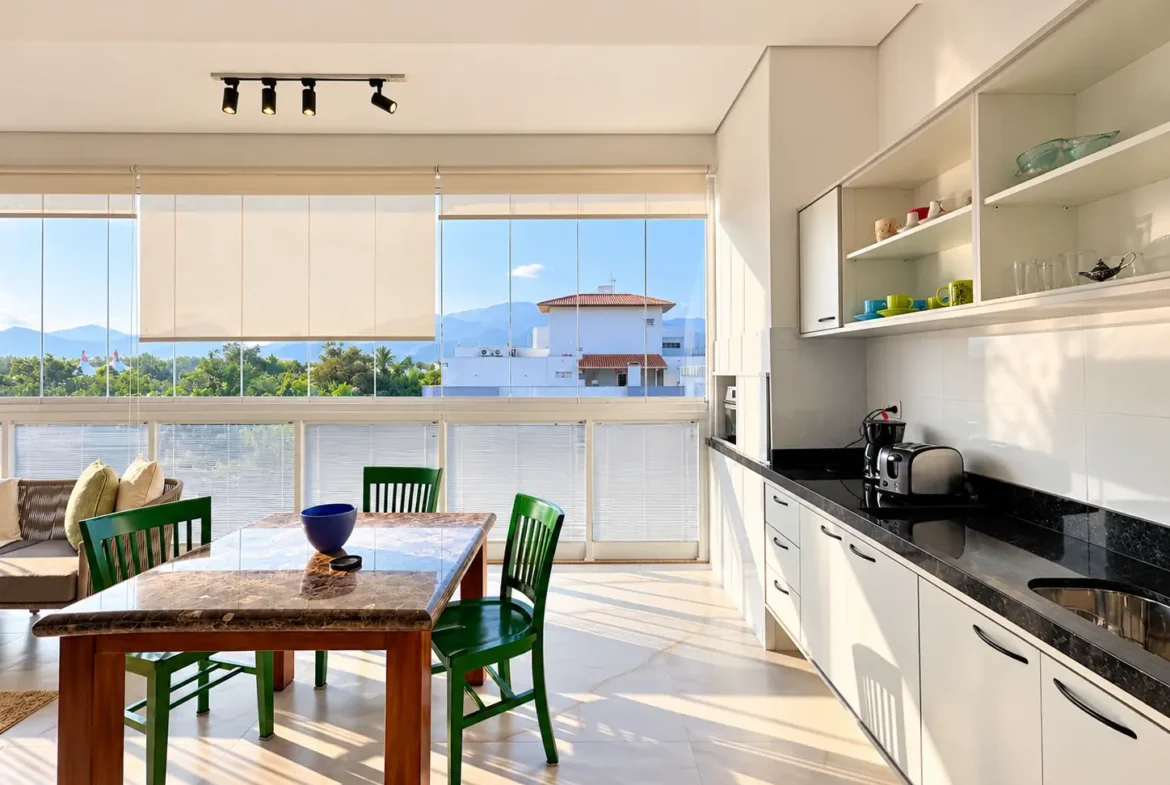 Cozinha planejada com bancada, armários claros, mesa de jantar e janela ampla.