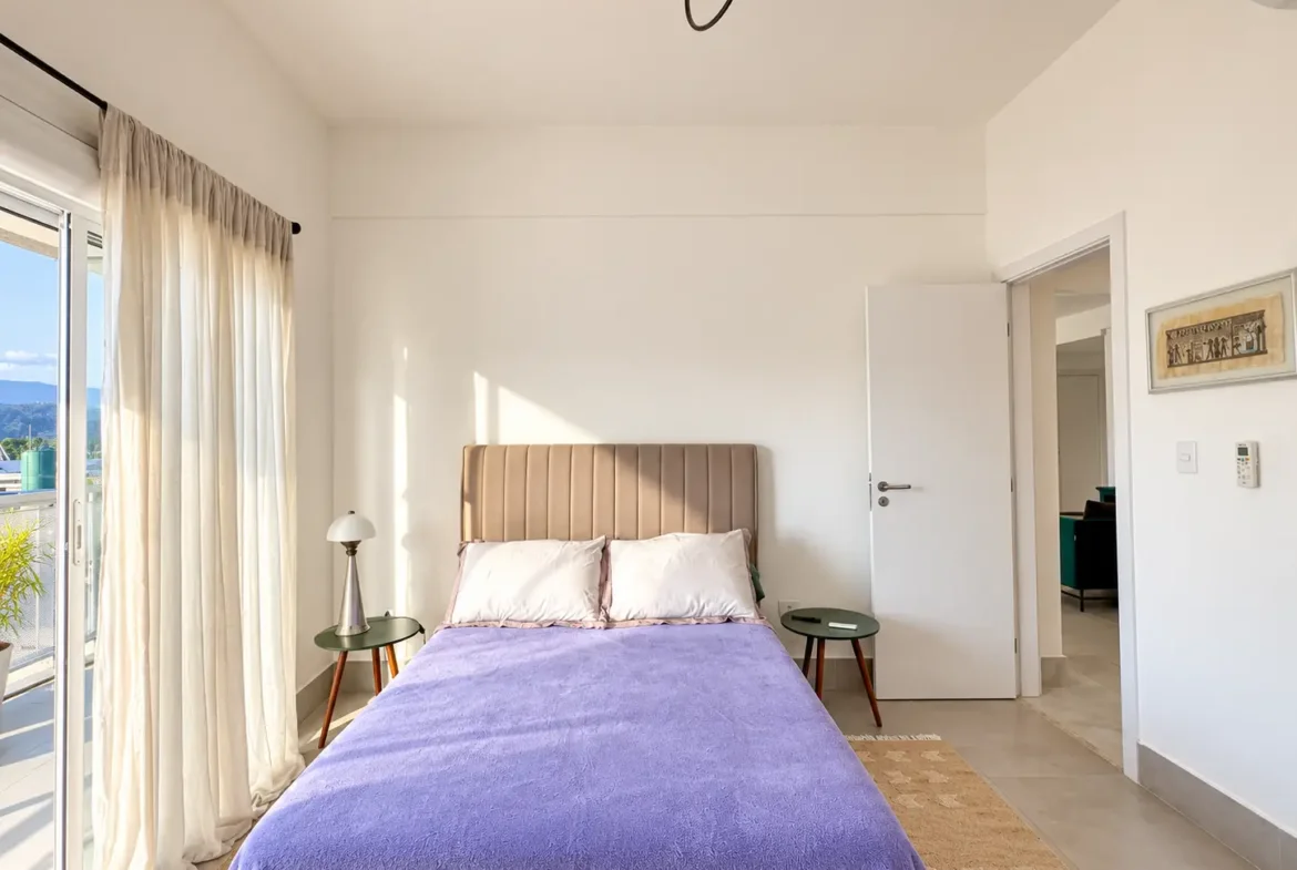 Dormitório com cama de casal, porta de vidro e acesso à varanda.