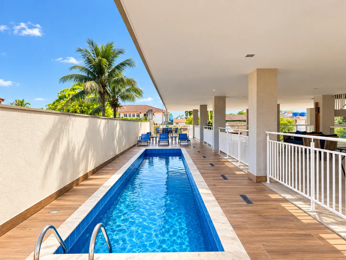 apartamento-itagua-lg117-113-82m2-piscina Piscina comprida na área externa do edifício, com deck, guarda-corpo de vidro e palmeiras.