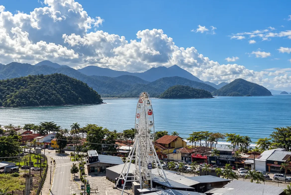 Vista elevada da região litorânea com roda-gigante, mar e montanhas ao fundo.