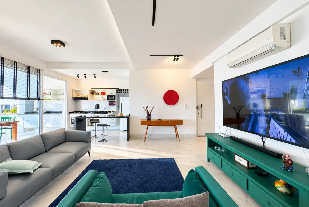 Sala de estar com sofás, televisão, parede decorativa e iluminação natural.
