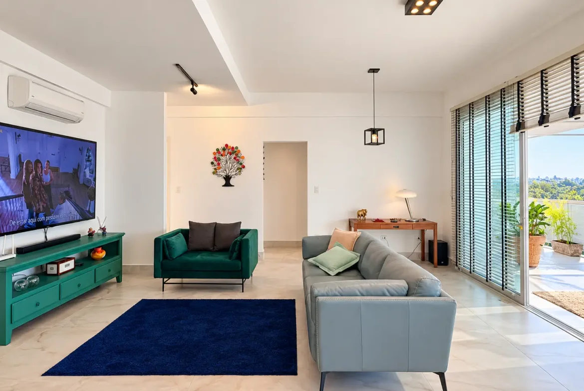 Sala de televisão com sofá, poltronas e porta de vidro de acesso à varanda.