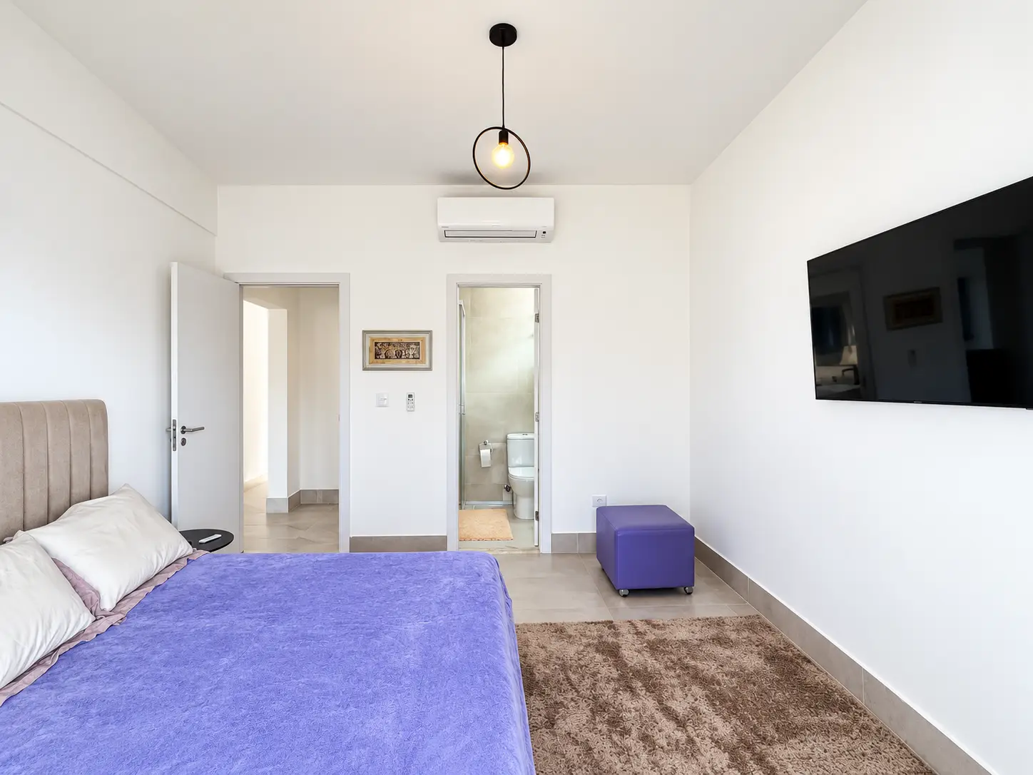 apartamento-itagua-lg117-113-82m2-suite-03 Vista da suíte com cama de casal, televisão na parede e circulação para os demais ambientes.