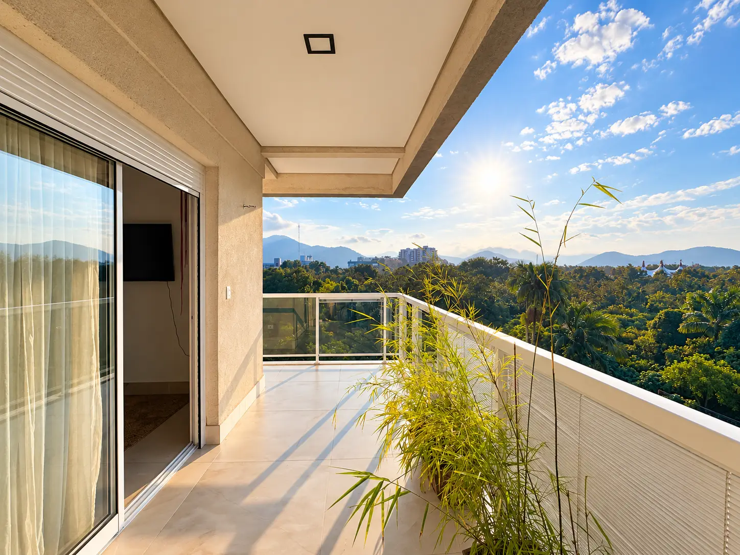 apartamento-itagua-lg117-113-82m2-varanda-ampla Varanda ampla com piso claro, guarda-corpo de vidro e vista para a vegetação e os morros.