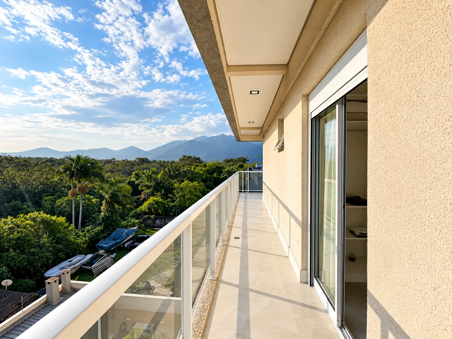 apartamento-itagua-lg117-113-82m2-varanda-dormitorio Varanda com guarda-corpo de vidro, portas de correr e vista para a vegetação.