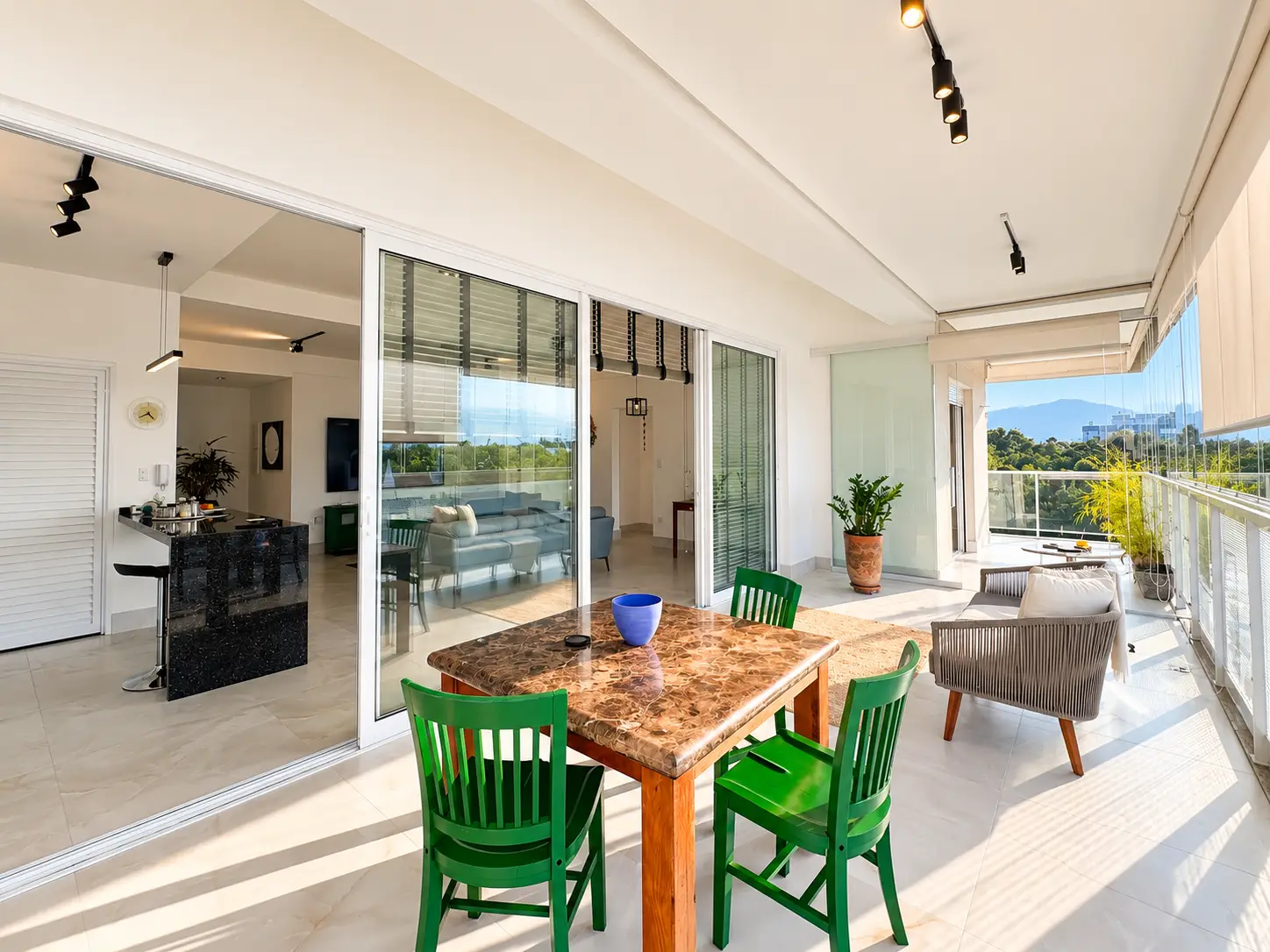 apartamento-itagua-lg117-113-82m2-varanda-integrada Varanda integrada à área social, com mesa de madeira, cadeiras e portas de vidro.