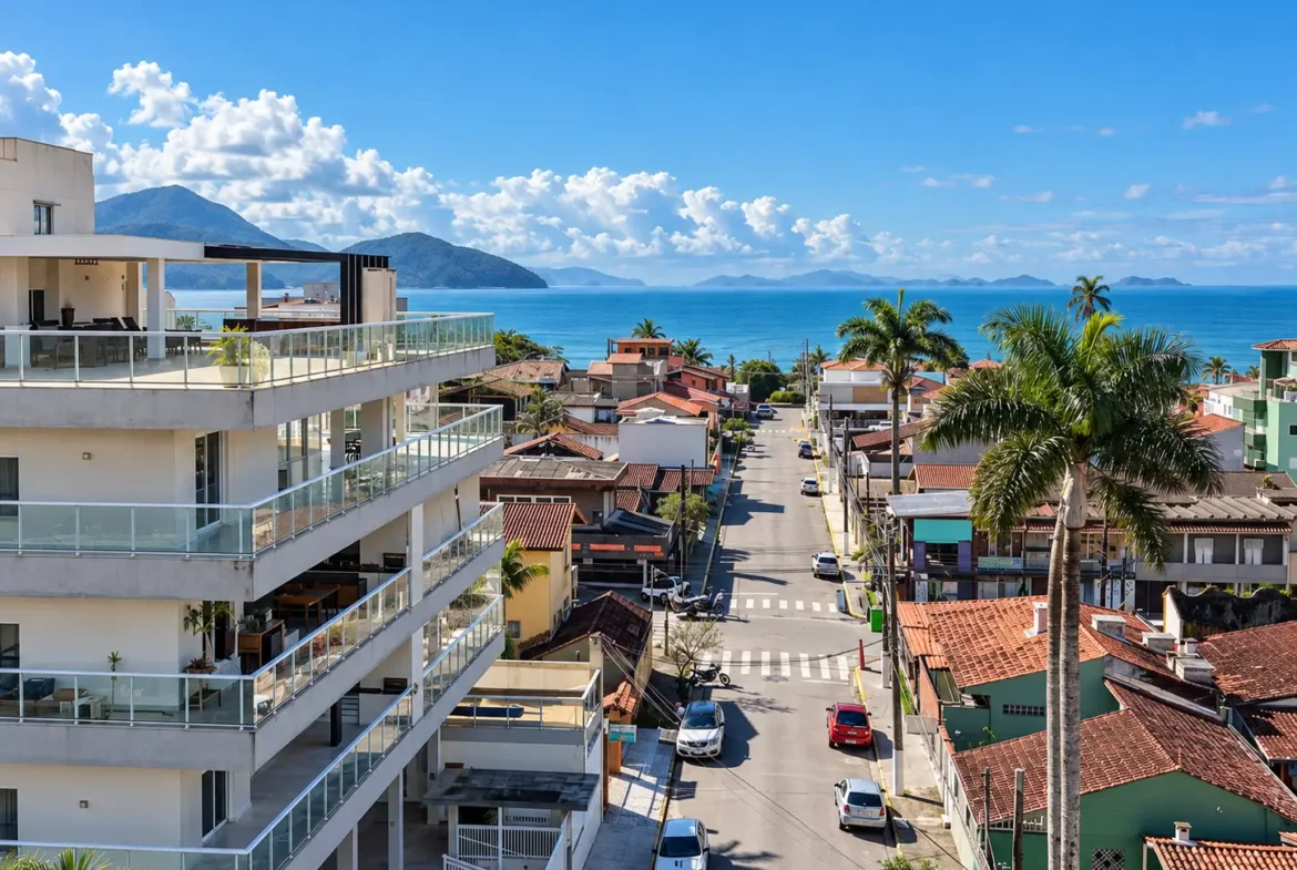 Vista elevada de rua com edifícios e palmeiras, com o mar e montanhas ao fundo.