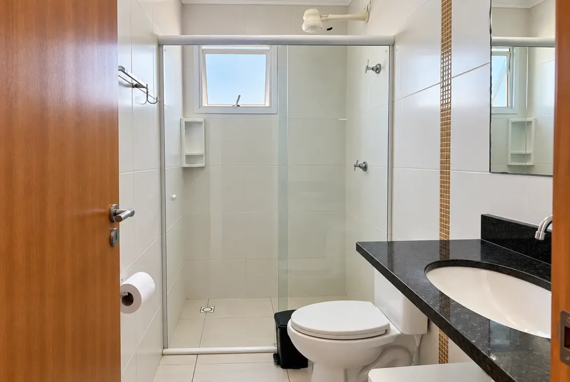Banheiro do apartamento com box de vidro, vaso sanitário e bancada com pia.