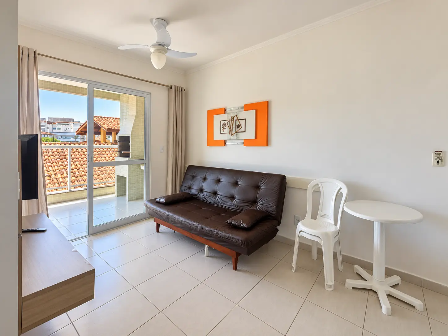 apartamento-praia-grande-sala-integrada Sala de estar com sofá, móveis e porta de vidro de acesso à varanda.