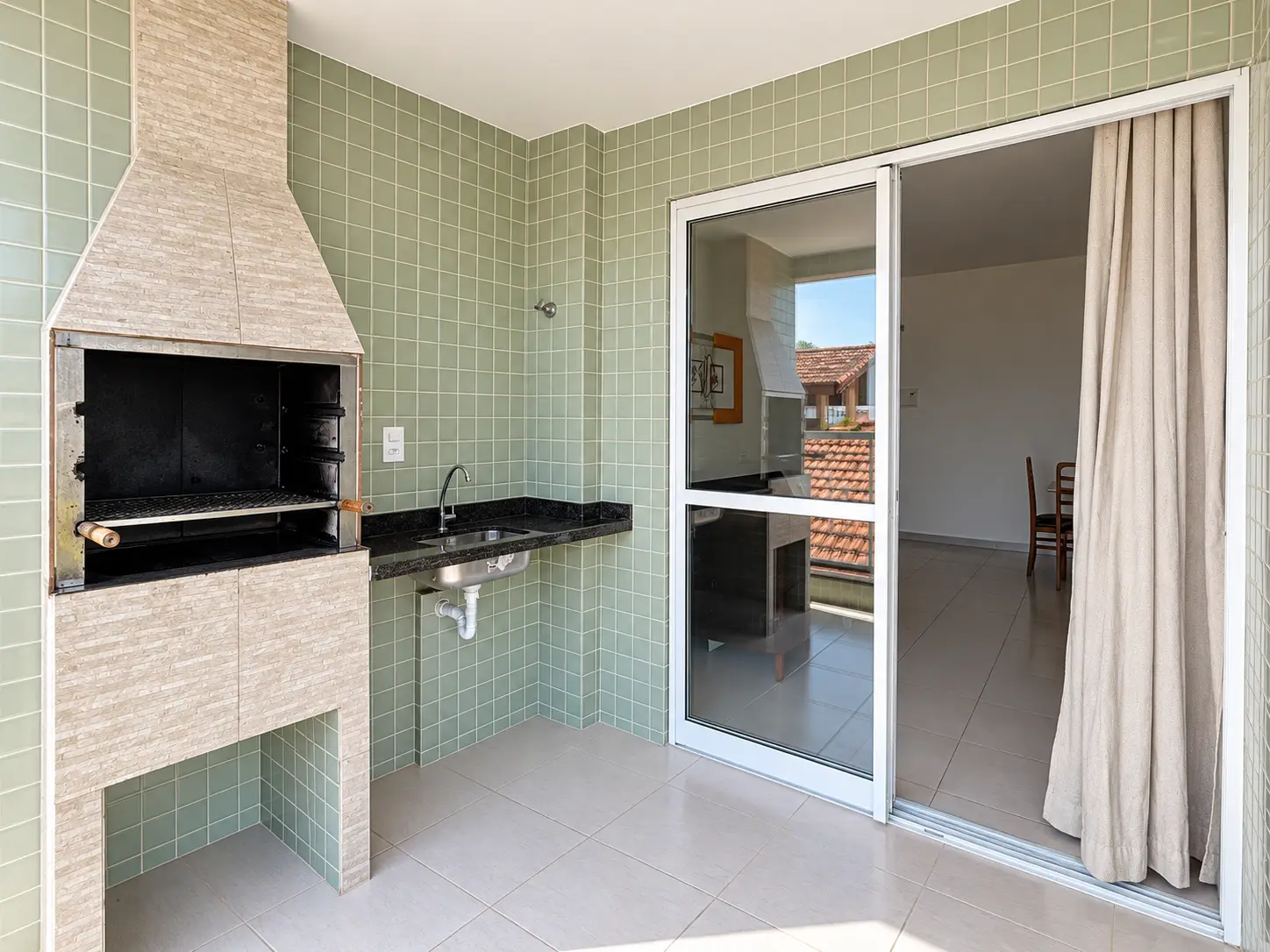 apartamento-praia-grande-varanda-gourmet-integrada Outro ângulo da varanda gourmet com churrasqueira, bancada e porta de vidro de acesso à sala.