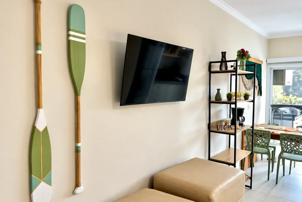 Ambiente da sala integrado do loft no Itaguá, com cama, sofá, televisão e móveis decorativos.