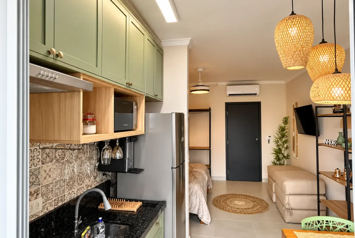 Vista da cozinha do loft integrada aos demais ambientes, com armários e iluminação pendente.
