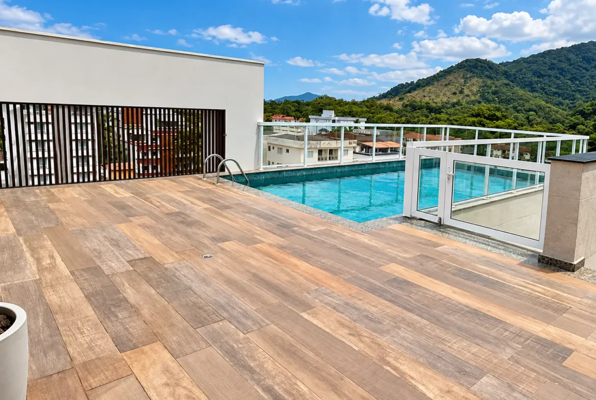 Área de lazer no rooftop com deck de madeira, piscina e vista para as montanhas.