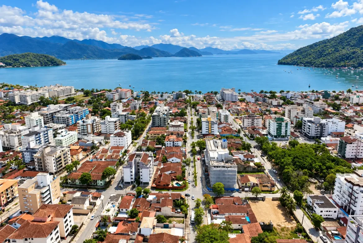 Vista aérea de região urbana do Itaguá, com construções, mar e montanhas ao fundo.