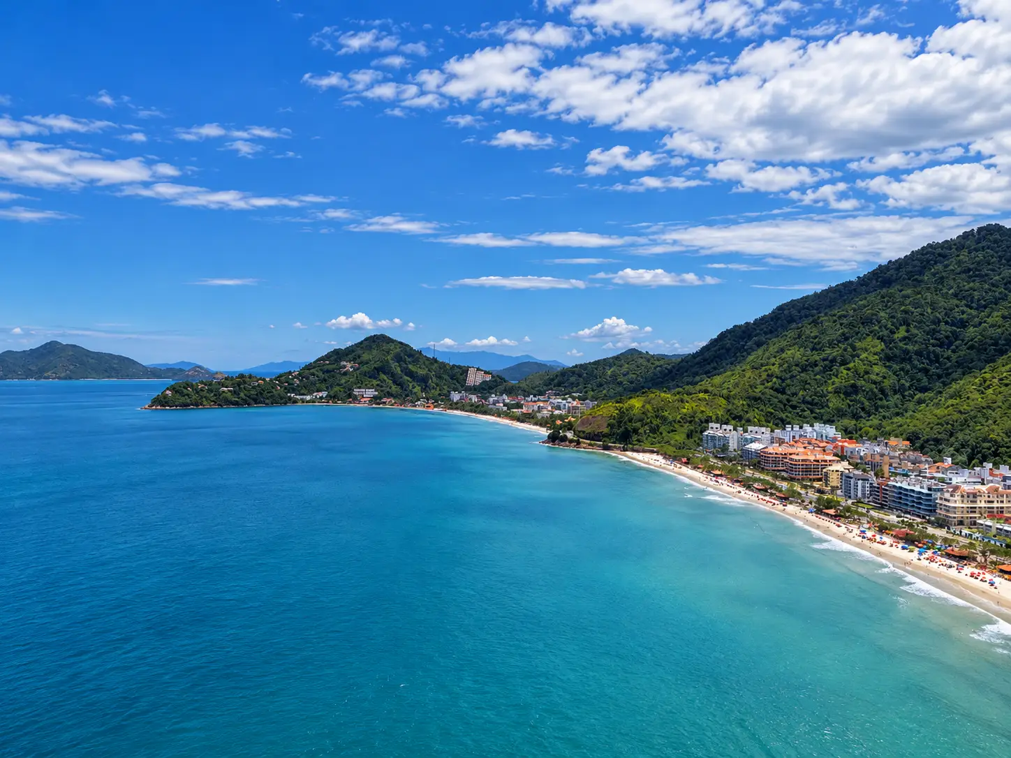 praia-grande-ubatuba-panorama-bairro Vista aérea da Praia Grande com mar azul, faixa de praia e encostas verdes.