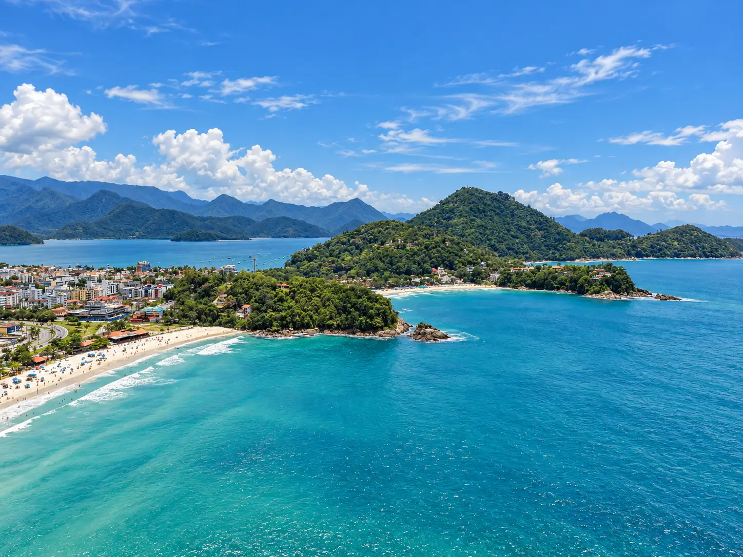 praia-grande-ubatuba-panorama-regiao Vista aérea de uma baía com águas azul-turquesa e morros cobertos por vegetação.
